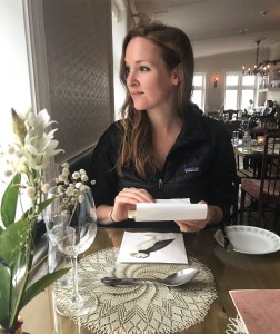 Woman sitting at a table looking out a window while holding a piece of paper.